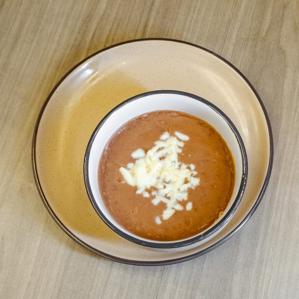Bowl of refried beans topped with shredded white cheese on a speckled plate.