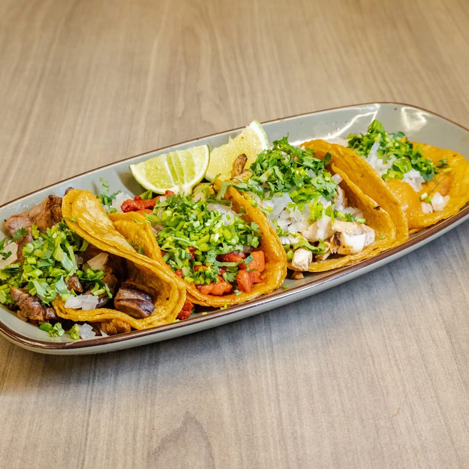Golden tacos filled with grilled meat, vegetables, onions, and cilantro on a platter with lime wedges.