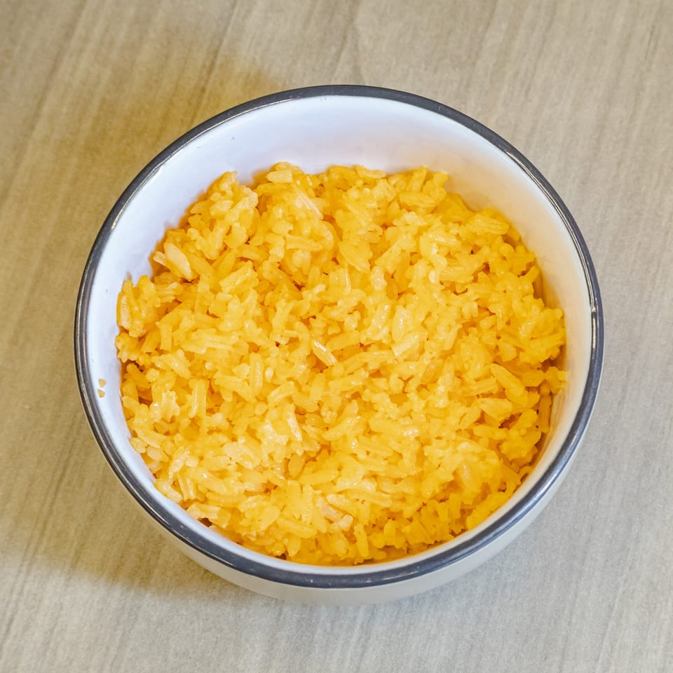 Bowl of vibrant yellow seasoned rice on a light wooden tabletop.