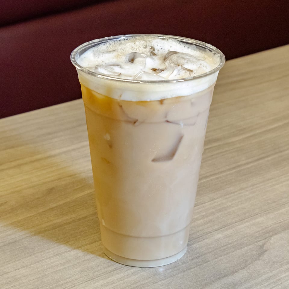 Iced creamy beverage with foam in a clear plastic cup on a wooden restaurant table.