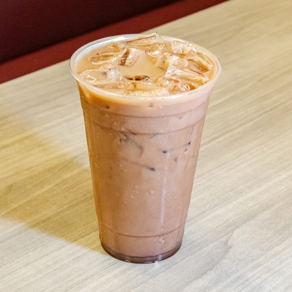 Iced coffee in a clear plastic cup sits on a light wooden table.