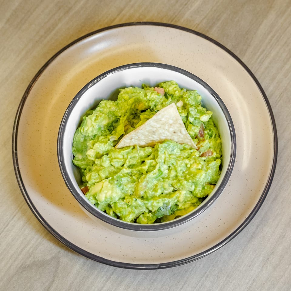 Bowl of chunky guacamole with tomato and cilantro, topped with a tortilla chip on a ceramic plate.
