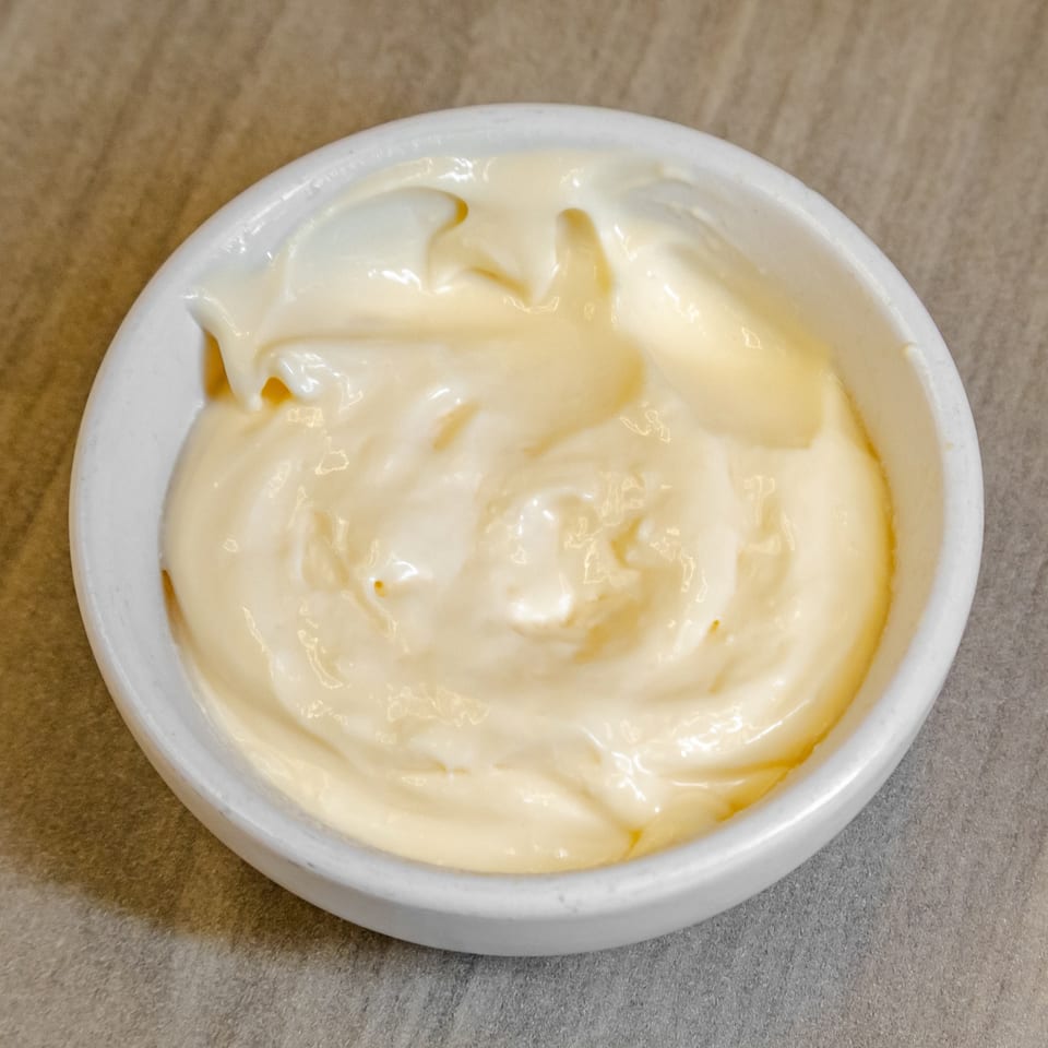 Small white bowl filled with creamy pale-yellow sauce on a tan restaurant table.