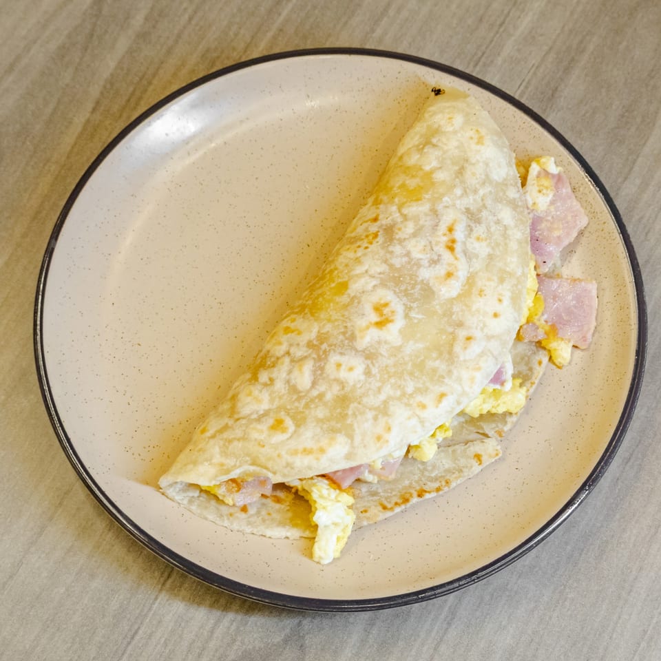 Folded breakfast quesadilla filled with scrambled eggs, ham, and melted cheese on a speckled ceramic plate.